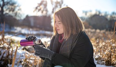Genç bir kadın, kışın yürüyüş yaparken termostan sıcak bir içecek alır..