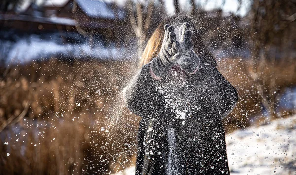 A woman throws snow on a walk in sunny weather in winter. — Stock Photo, Image