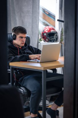 Kulaklık takan yorgun bir genç odasında dizüstü bilgisayarın önünde oturuyor..