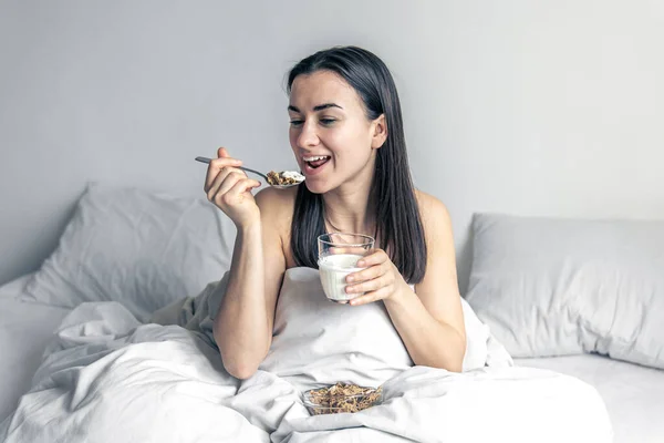 Una joven en cama blanca con cereales y leche. — Foto de Stock