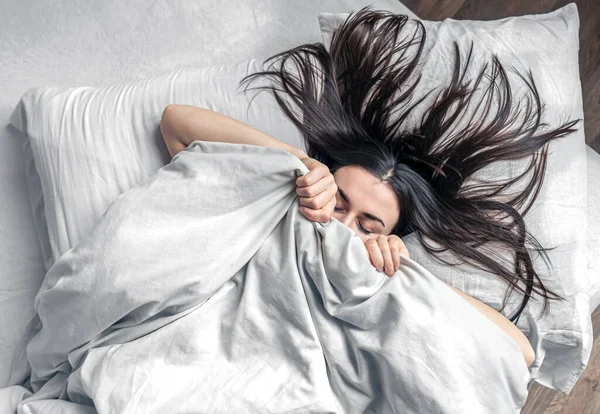 Una hermosa joven duerme en una cama blanca. — Foto de Stock