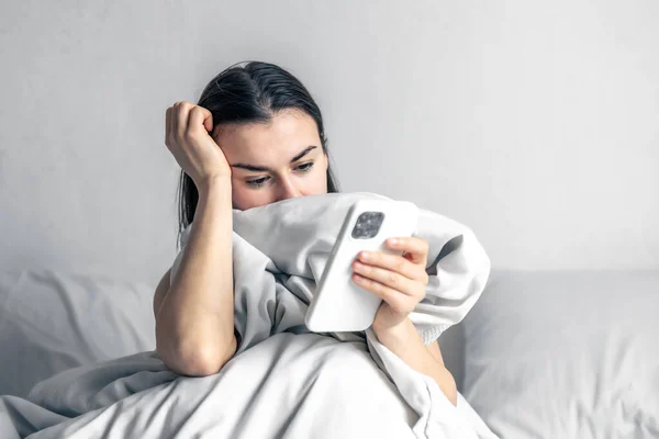 O femeie tânără în pat cu smartphone dimineața. — Fotografie, imagine de stoc