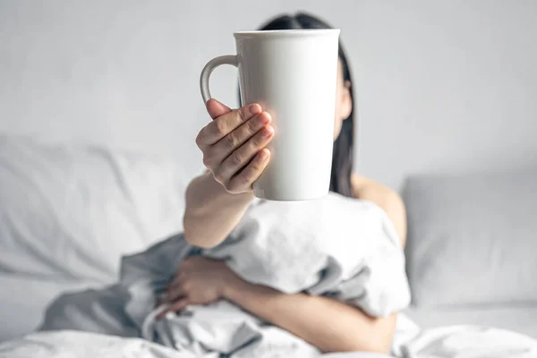Una mujer sostiene una taza de café mientras está en la cama. — Foto de Stock