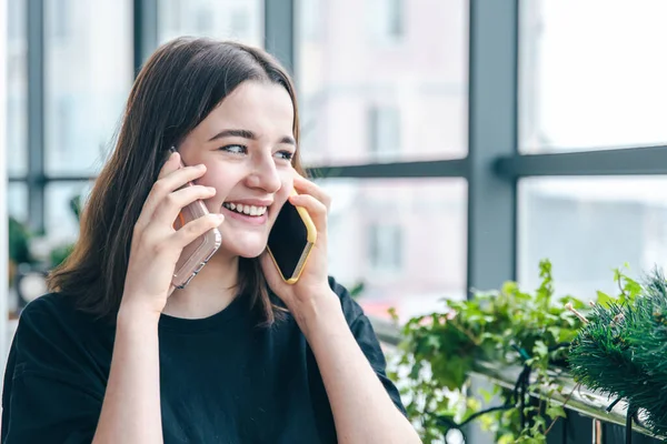 Retrato de una joven sonriente hablando por dos teléfonos. — Foto de Stock