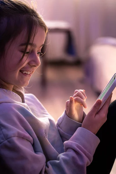Ein kleines Mädchen benutzt ein Smartphone, während es in ihrem Zimmer sitzt. — Stockfoto