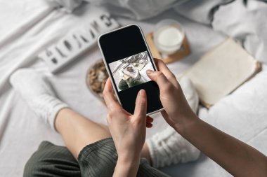 Bir kadın yatakta yatarken kahvaltının fotoğrafını çeker..