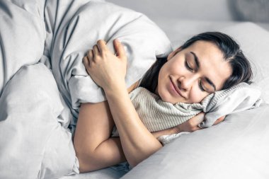 Güzel genç bir kadın beyaz bir yatakta uyuyor..