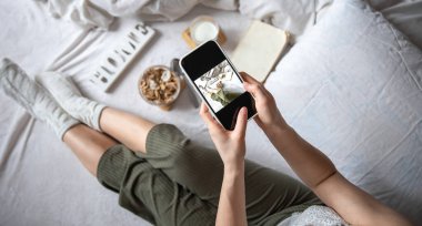 Bir kadın yatakta yatarken kahvaltının fotoğrafını çeker..