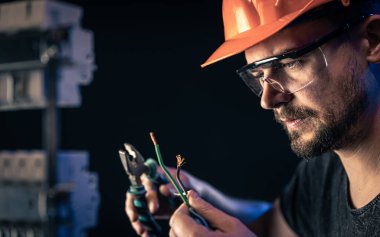 Bir erkek elektrikçi elektrik kablosuyla santralde çalışıyor..