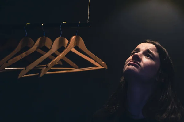 Seorang wanita muda dekat hangers kosong dalam gelap di bawah lampu. — Stok Foto