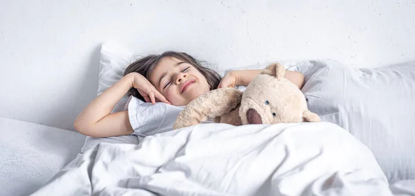 Kleine süße Mädchen im Bett mit einem Teddybär am frühen Morgen. — Stockfoto