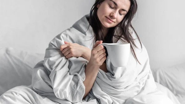 Una hermosa joven en una cama blanca con una taza de café. — Foto de Stock