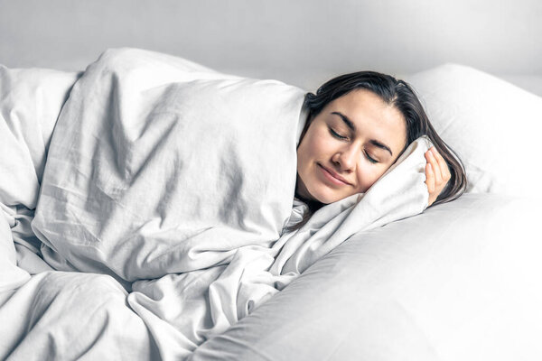 A beautiful young woman sleeps in a white bed.