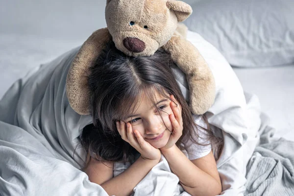 Маленька мила дівчинка в ліжку з плюшевим ведмедем рано вранці . — стокове фото