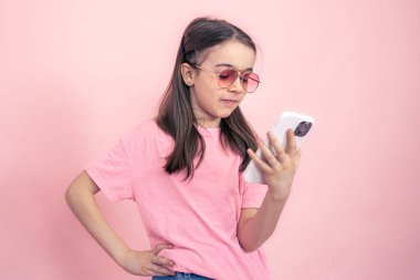 Pembe arka planda akıllı telefonu olan şık küçük bir kız..