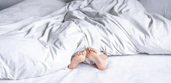 小さな女の子の足は白い毛布の下から突き出て. — ストック写真