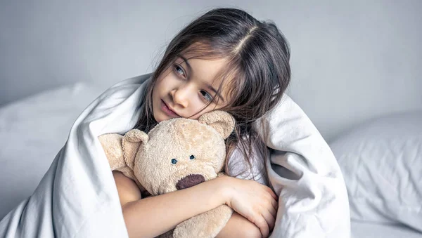 Μικρό χαριτωμένο κορίτσι στο κρεβάτι με ένα αρκουδάκι νωρίς το πρωί. — Φωτογραφία Αρχείου