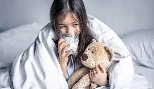 Ένα μικρό χαριτωμένο κορίτσι στο κρεβάτι με βελούδινο και ένα ποτήρι γάλα. — Φωτογραφία Αρχείου