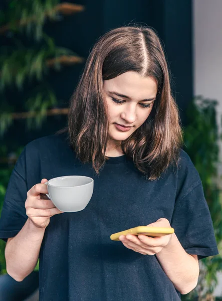 Adolescente con una taza de té y un teléfono inteligente en las manos. — Foto de Stock