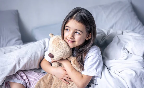 Νυσταγμένο κοριτσάκι με το αγαπημένο της αρκουδάκι στο κρεβάτι το πρωί. — Φωτογραφία Αρχείου