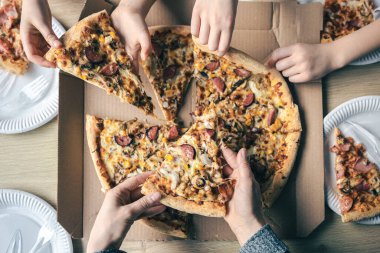 Masadaki karton kutudan pizza dilimleri alan gençler..