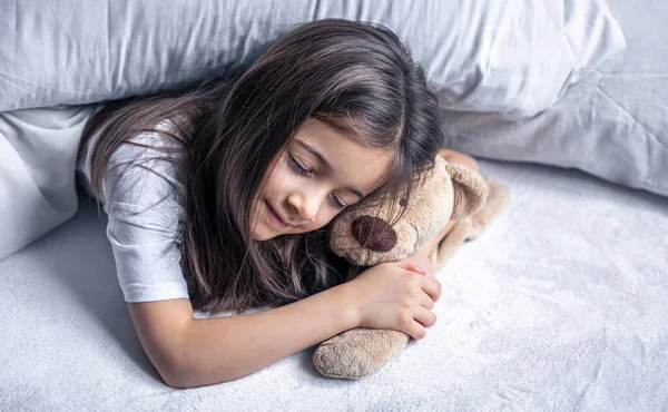 Маленька мила дівчинка в ліжку з плюшевим ведмедем рано вранці . — стокове фото