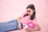 Stylová holčička s chytrým telefonem na růžovém pozadí.