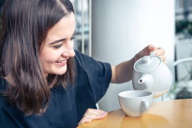 Genç bir kadının yakın çekimi çaydanlıktan çay doldurur..