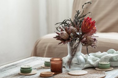 Mumlar ve protea buketiyle rahat ev kompozisyonu.