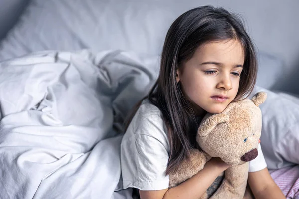 Νυσταγμένο κοριτσάκι με το αγαπημένο της αρκουδάκι στο κρεβάτι το πρωί. — Φωτογραφία Αρχείου