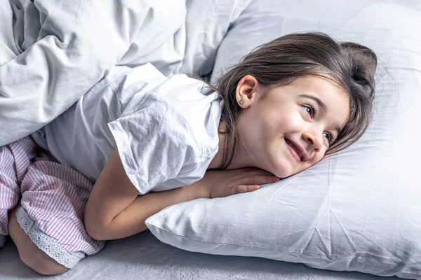 Ένα χαριτωμένο κοριτσάκι ξαπλώνει στο κρεβάτι και δεν θέλει να σηκωθεί.. — Φωτογραφία Αρχείου