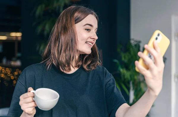 Una adolescente con una taza de té y un teléfono inteligente en las manos. — Foto de Stock