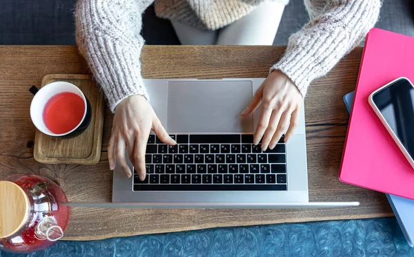 Kobieta pracująca na laptopie w kawiarni z filiżanką herbaty, widok z góry. — Zdjęcie stockowe
