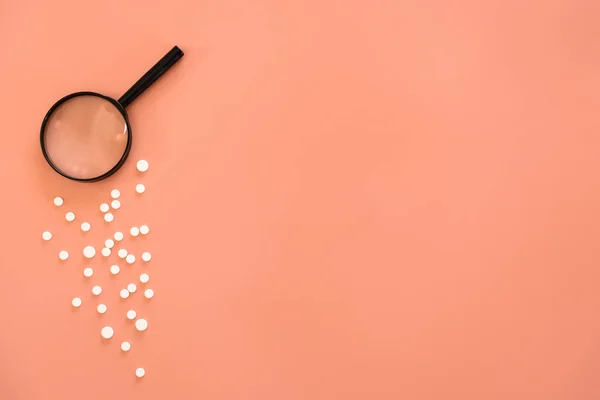 Flat lay, pills and magnifier on pink background, copy space. — Stock Photo, Image