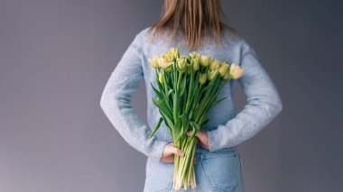 Bir kadın arkasında gri bir arka planda bir buket lale tutuyor..