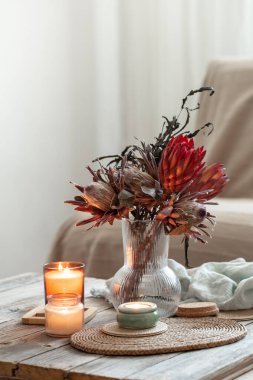 Mumlar ve protea buketiyle rahat ev kompozisyonu.