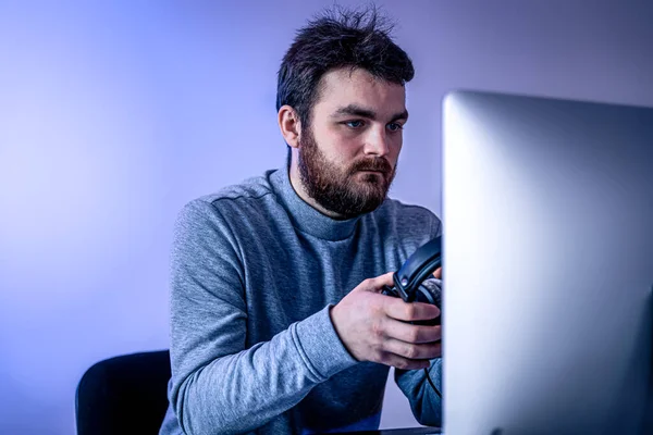Un hombre se sienta frente a una computadora, sosteniendo auriculares en sus manos. — Foto de Stock