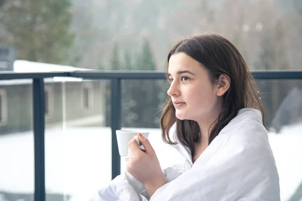 Une jeune femme avec une tasse de café sur le balcon en hiver dans les montagnes. — Photo