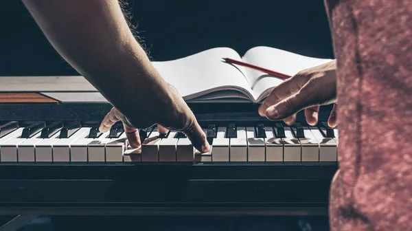 Ein Mann spielt Klavier und schreibt im Dunkeln in ein Notizbuch. — Stockfoto