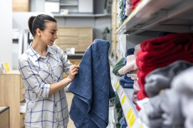 Malzeme dükkanındaki genç bir kadın mavi bir banyo havlusu seçiyor..