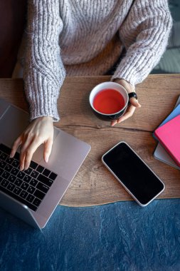 Bir kafede dizüstü bilgisayarda çalışan bir kadın, bir fincan çay, üst manzara..