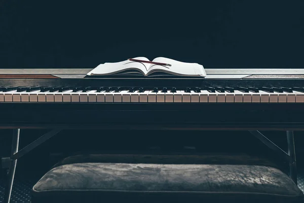 Открытый блокнот на клавишах пианино в темноте, пространство для копирования. — стоковое фото