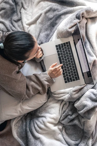 Uma mulher trabalhando em um laptop enquanto deitada na cama, vista superior. — Fotografia de Stock