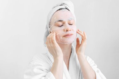 Yüzünde çarşaf maskesi olan genç bir kadın, spa prosedürü..