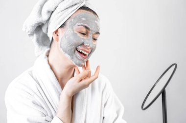 Aynanın önünde yüzünde kilden bir maske olan genç bir kadın..