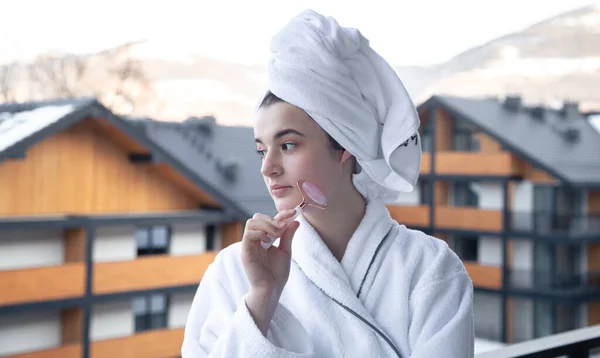 Eine junge Frau mit einem Handtuch auf dem Kopf macht eine Massage mit einer Gesichtsrolle. — Stockfoto