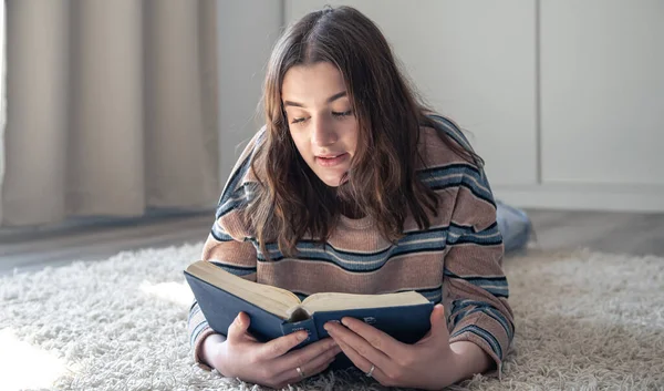 Una joven leyendo un libro tumbada en el suelo en casa. — Foto de Stock