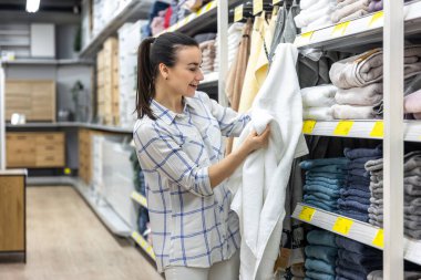 Malzeme dükkanındaki genç bir kadın mavi bir banyo havlusu seçiyor..