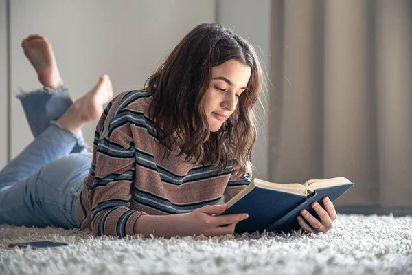 Genç bir kadın odasında yerde otururken bir kitap okuyor.. — Stok fotoğraf