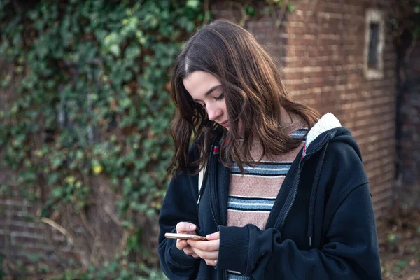 Eine junge Frau benutzt ein Telefon auf dem Hintergrund einer Wand mit Efeu. — Stockfoto
